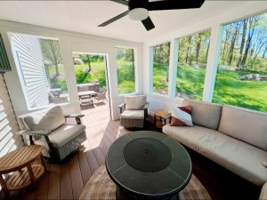 Screened porch with cushioned seating, ceiling fan, and garden view