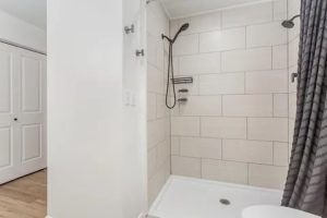 Tub–shower with large subway tile, matte-black showerhead and handheld, white tub, and dark curtain.