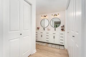 Entry view with white double doors, wood-look floor, and a double vanity with round mirrors