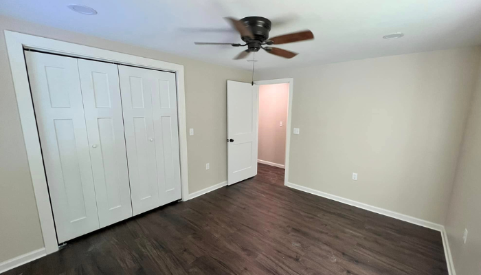 renovated new bedroom with light walls, white closet doors dark wood floor