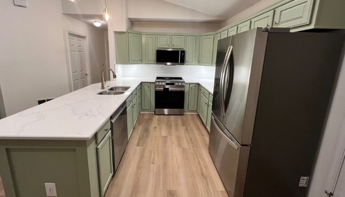 newly renovated kitchen with light wood floor and light green cabinets and stainless steel appliances