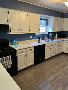 kitchen with medium wood floor white cabinets white counters black appliances white farm sink